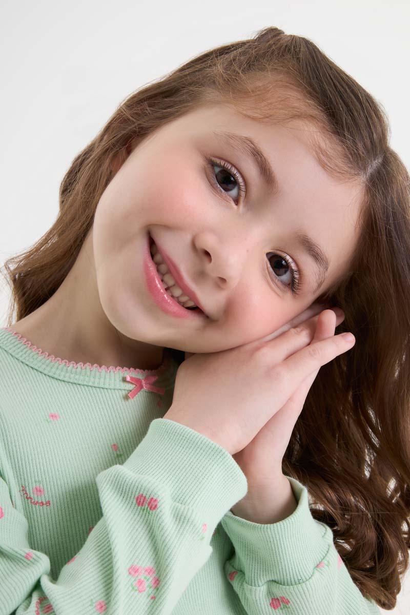 Menina sorrindo usando pijama infantil de manga longa verde com estampa de flores